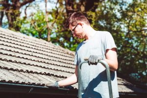 Young adult cleaning leaves from a gutter on a high ladder, chores, taking care of home