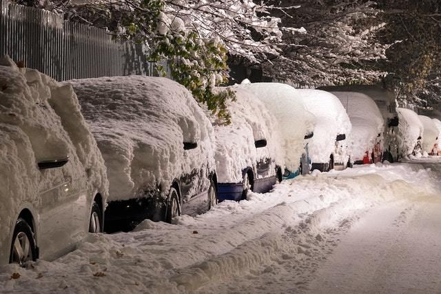 Snow covered cars parked on street.