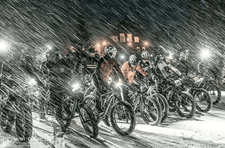 Fat tire bikers waiting for the race to start at night as snow pours down